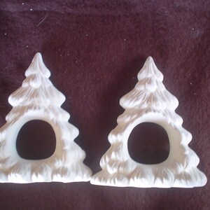May include: Two white ceramic Christmas tree napkin rings. The rings are shaped like a Christmas tree with a hole in the center for a napkin.
