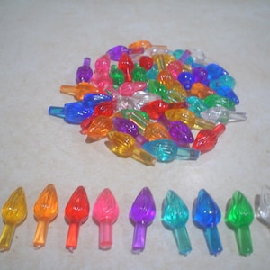 May include: Assortment of colorful plastic Christmas light bulb covers in various colors, including red, orange, yellow, green, blue, purple, and clear. The covers are arranged in a circle on a white surface. There are also 10 individual covers lined up in a row below the circle.