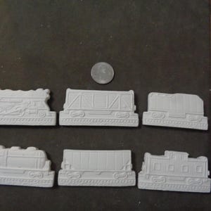 May include: Six white ceramic train car ornaments, including a locomotive, boxcar, flatcar, and caboose. The ornaments are ready to be painted.