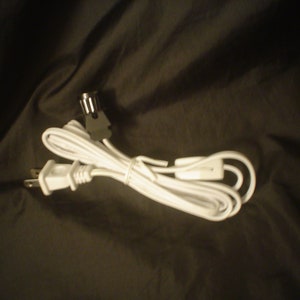 May include: White electrical cord with a plug on one end and a switch on the other end.