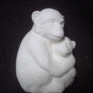 May include: White ceramic figurine of two monkeys hugging. The larger monkey is sitting with its arms wrapped around the smaller monkey. Both monkeys have closed eyes and are smiling.