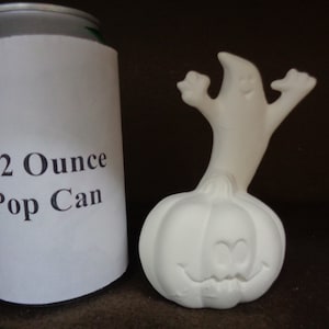 May include: White ceramic pumpkin with a ghost on top. The pumpkin has a carved jack-o'-lantern face. The ghost has arms raised in the air. The pumpkin is about the size of a 12-ounce pop can.