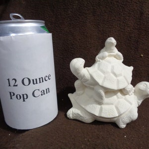 May include: A white ceramic figurine of three turtles stacked on top of each other. The turtles are all facing forward and have their heads up. The figurine is about the size of a 12-ounce pop can.