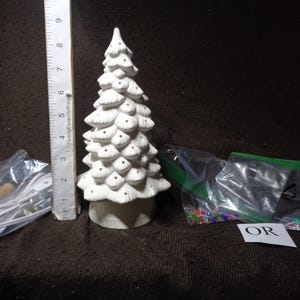 May include: A white ceramic Christmas tree with a textured surface and small black dots. The tree is approximately 8 inches tall. Accessories include a ruler, small lights, and colorful beads. The tree is unpainted and ready for customization.
