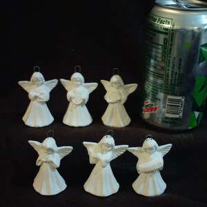 May include: Six white ceramic angel ornaments with different poses and musical instruments. The angels are about 2 inches tall and are shown next to a soda can for size comparison.