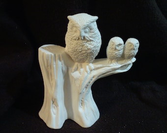 May include: A white ceramic owl family figurine with three owls perched on a tree stump. The owls have detailed features and are posed in a natural setting.