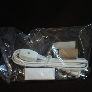 May include: A white electrical cord with a white inline switch and a white plug. The cord is packaged in a clear plastic bag with a brown cardboard electrical socket.