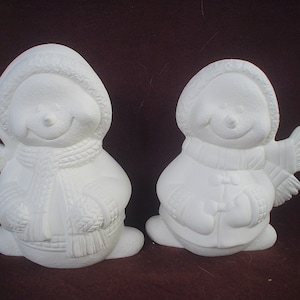 May include: Two white ceramic snowman figurines with smiling faces. One snowman is wearing a scarf and hat, while the other is wearing a coat and hat.