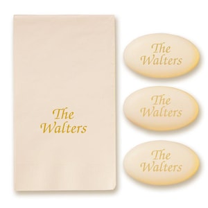 May include: A cream-colored towel and three oval soaps, all with the text "The Walters" in a gold script. The towel is rectangular and folded, with the text printed near the bottom. The soaps are light yellow and have a smooth surface.