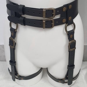 Puede incluir: Cintur&oacute;n de liga de cuero negro con dos filas de hebillas y dos correas con anillos y hebillas.