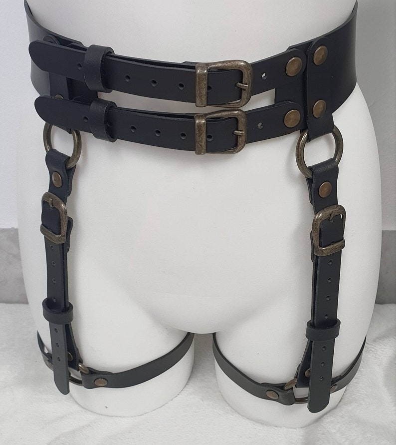 Puede incluir: Cintur&oacute;n de liga de cuero negro con dos filas de hebillas y dos correas con anillos y hebillas.