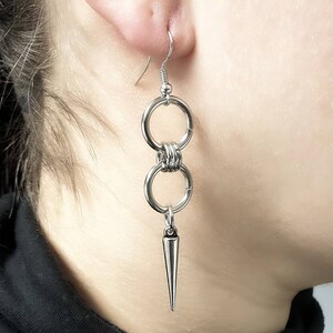 May include: Silver earrings with two connected rings and a pointed spike hanging from the bottom.