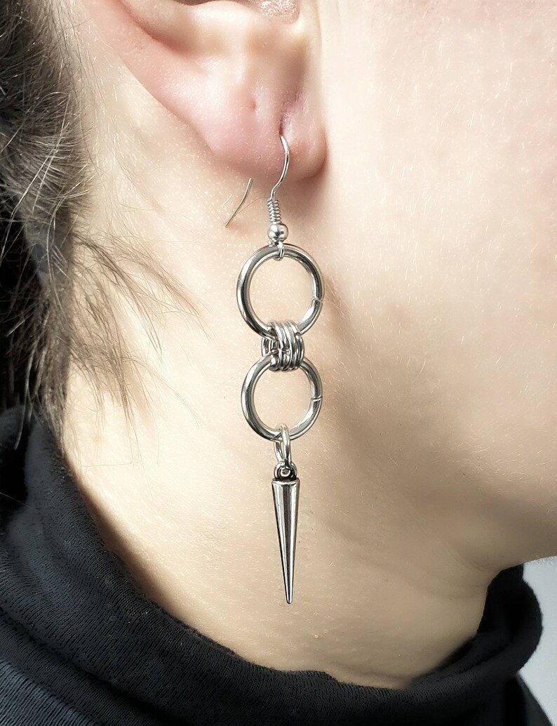 May include: Silver earrings with two connected rings and a pointed spike hanging from the bottom.