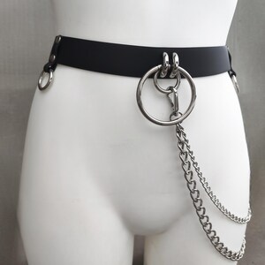 May include: A black belt featuring silver-toned metal hardware, including a large central ring, two smaller rings on the sides, and a double-layered silver chain attachment that hangs from the front ring, secured with a lobster claw clasp.