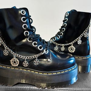 May include: Black leather platform boots with silver chains and pentagram charms. The boots have a chunky platform sole and lace-up closure.