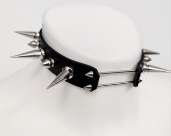 May include: A black leather choker with silver spikes. The choker has two rows of spikes and a metal buckle.