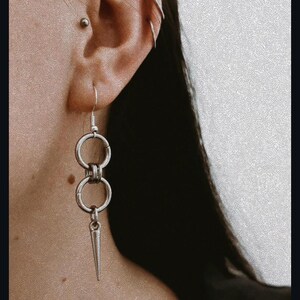 May include: Silver dangle earrings with two connected rings and a pointed spike charm.