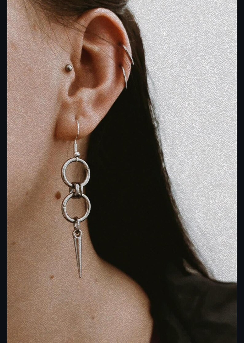 May include: Silver dangle earrings with two connected rings and a pointed spike charm.