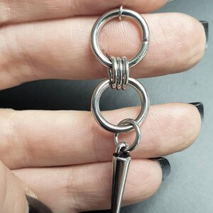 May include: Silver double hoop earring with a sharp, pointed spike charm hanging from the bottom.