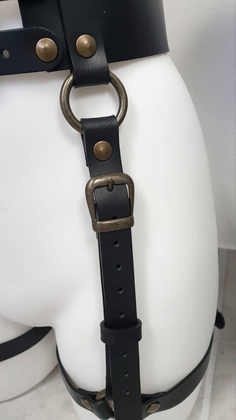 Puede incluir: Arn&eacute;s de cuero negro con hebilla de metal y anillo en D. El arn&eacute;s tiene m&uacute;ltiples correas y es ajustable.