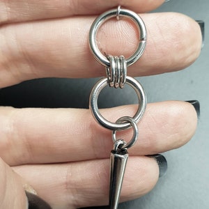 May include: Silver hoop earrings with a dangling spike charm. The hoops are connected by a smaller hoop.