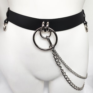 May include: A black belt featuring a large silver-toned metal ring at the center, connected to two smaller silver rings. A double-layered silver chain hangs from the central ring. The belt also includes silver-toned metal rings at each side.