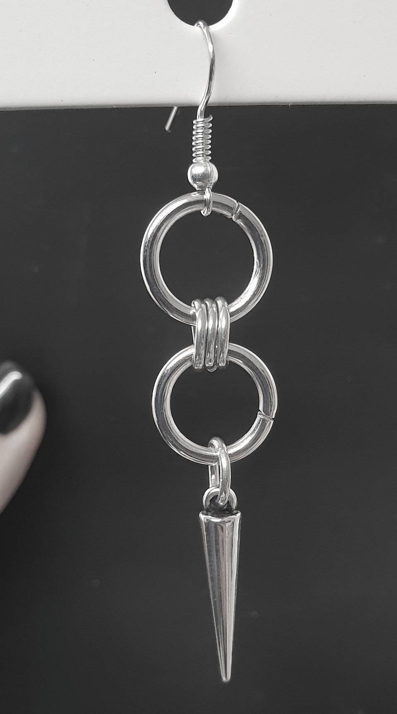 May include: Silver dangle earrings with two connected circles and a pointed spike charm.