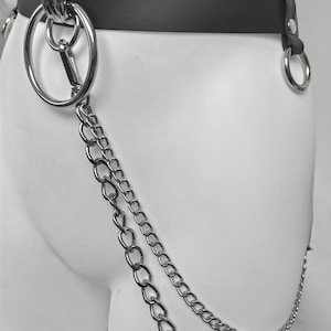 May include: A black belt featuring a large silver-toned metal O-ring attached to the front, with a double-layered silver chain hanging from the ring. The belt is secured with silver-toned rivets and includes an additional side O-ring attachment.