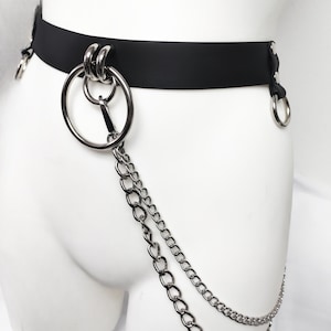 May include: A black belt featuring silver-toned metal hardware, including a large circular ring at the front and smaller rings on the sides. Two silver-toned metal chains of varying lengths hang from the front ring, creating a layered effect.