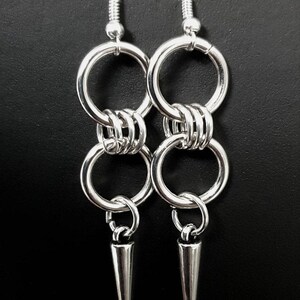 May include: Silver dangle earrings with two connected rings and a pointed spike at the bottom.