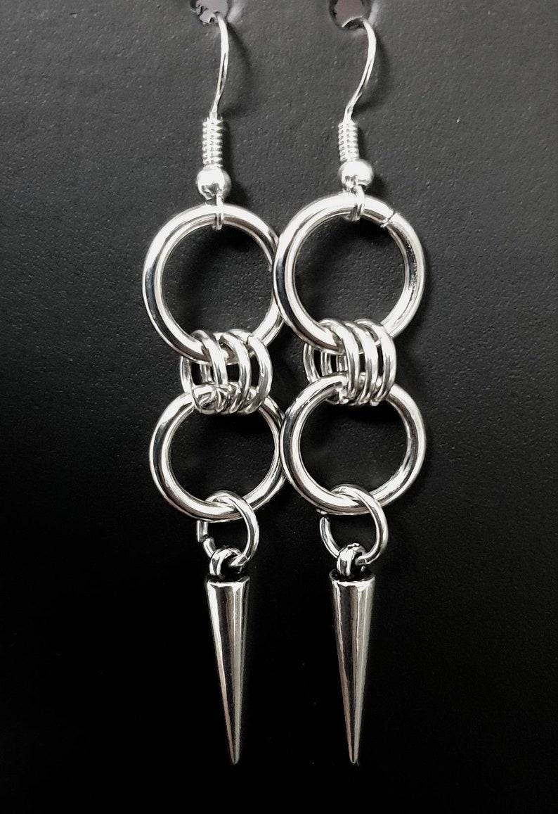 May include: Silver dangle earrings with two connected rings and a pointed spike at the bottom.