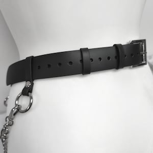 May include: A black belt featuring a silver-toned metal buckle and a series of adjustment holes. The belt includes two fixed loops and a silver-toned metal ring attached to a side strap, which connects to a dangling silver-toned metal chain.