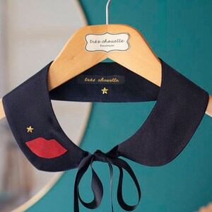 May include: A black fabric collar with a red lip and gold star embellishments. The collar is on a wooden hanger with a label that reads "tres chouette handmade".