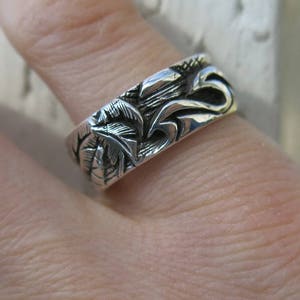 May include: A silver ring with a detailed design of leaves and swirls.
