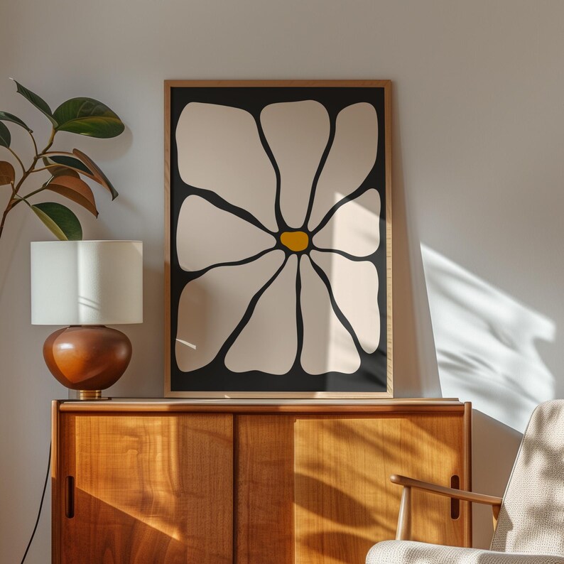 May include: A framed art print featuring a large, stylized flower. The flower has cream-colored petals outlined in black, with a yellow center, set against a black background. The artwork is displayed in a wooden frame.