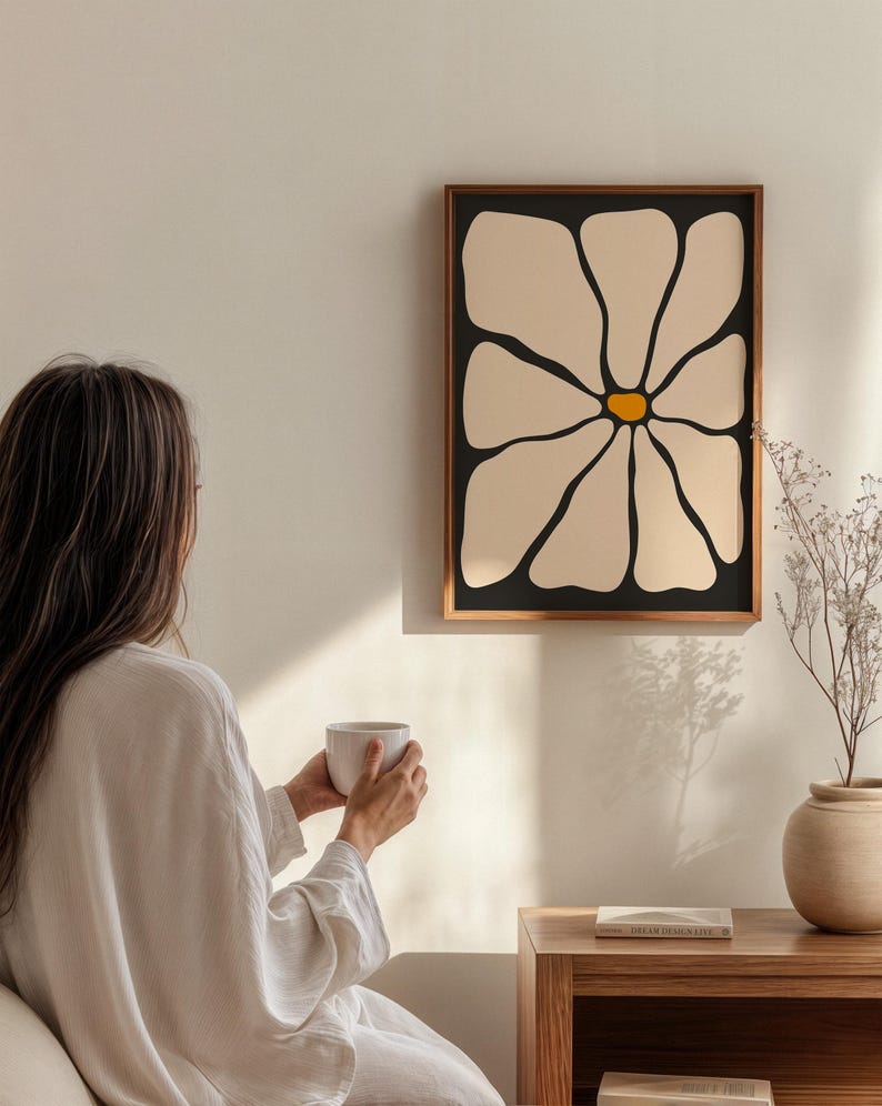 May include: A framed wall art print featuring a large, stylized daisy flower with cream-colored petals and a yellow center against a black background. The artwork is in a dark brown wooden frame. The image is a minimalist, modern design.