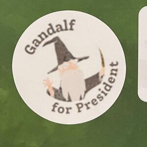 May include: A white circle sticker with a cartoon image of Gandalf from the Lord of the Rings, wearing a black pointed hat and holding a staff. The text "Gandalf for President" is written around the image.