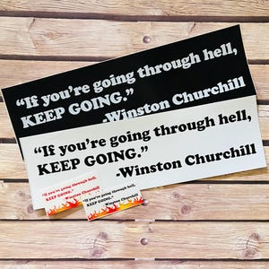 May include: Two black and white motivational quote stickers with the text "If you're going through hell, KEEP GOING." attributed to Winston Churchill. The stickers are on a wooden surface.