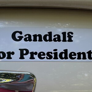 May include: A white bumper sticker with black text that reads "Gandalf for President".