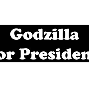 May include: A rectangular black sign featuring the white text Godzilla for President in a bold, rounded serif font. The text is arranged in two lines, with Godzilla on the top line and for President on the bottom line, centered on the black background.