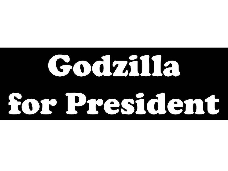 May include: A rectangular black sign featuring the white text Godzilla for President in a bold, rounded serif font. The text is arranged in two lines, with Godzilla on the top line and for President on the bottom line, centered on the black background.