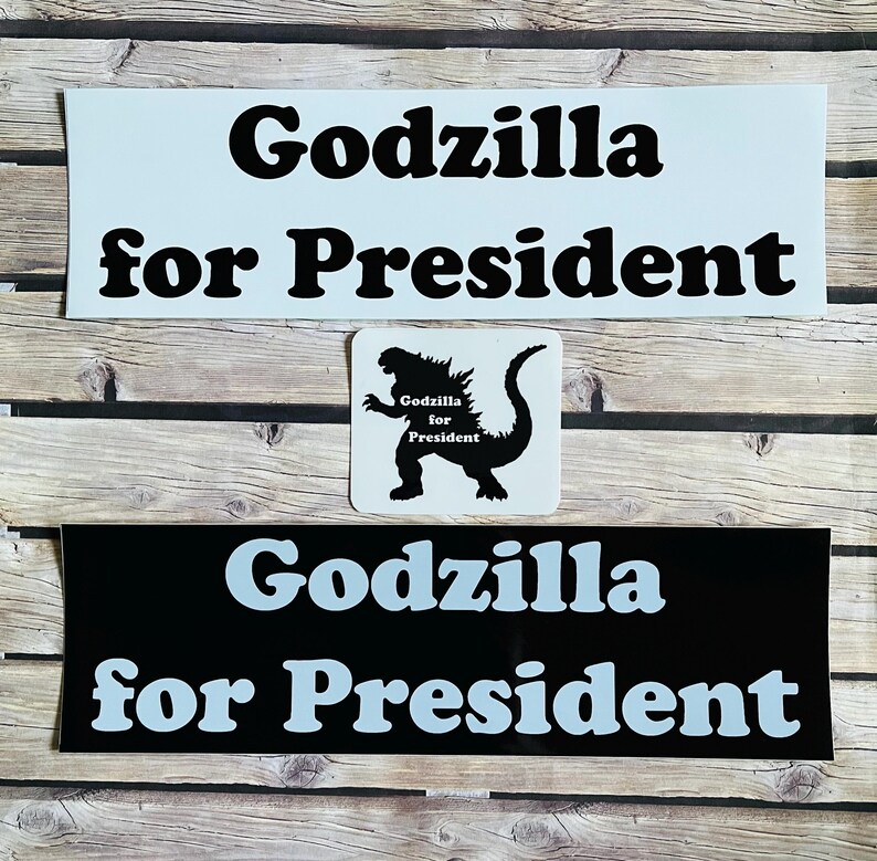 May include: Three rectangular and square stickers featuring the text Godzilla for President. One sticker is white with black text, one is black with light blue text, and a square sticker shows a black Godzilla silhouette with the text inside.