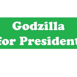 May include: A rectangular green sign featuring the white text Godzilla for President in a bold, serif font. The design is centered on the solid green background, presenting the phrase clearly in two lines with the word Godzilla above for President.