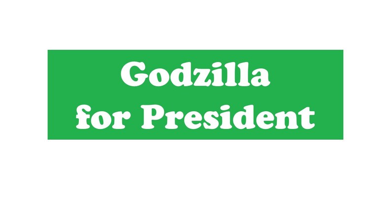 May include: A rectangular green sign featuring the white text Godzilla for President in a bold, serif font. The design is centered on the solid green background, presenting the phrase clearly in two lines with the word Godzilla above for President.
