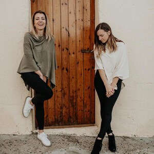 Peut inclure: Deux personnes portant des ponchos, l'un en vert et l'autre en blanc, se tiennent devant une porte en bois. Elles portent toutes les deux un pantalon noir et des chaussures.