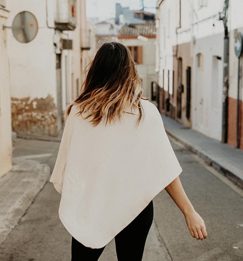 Peut inclure: Une femme portant un poncho blanc et un pantalon noir marche dans une rue &eacute;troite.