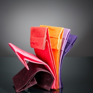 May include: A collection of folded fabric pouches arranged in a vertical fan shape. The pouches feature a vibrant gradient of colors including deep burgundy, bright pink, red, orange, light purple, and dark violet, each with a rectangular flap.