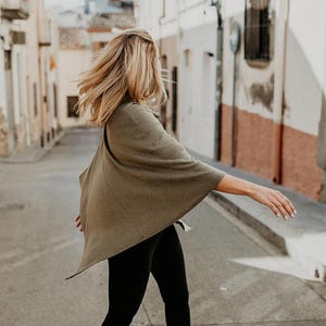 Peut inclure: Une femme portant un poncho vert et un legging noir marche dans une rue.