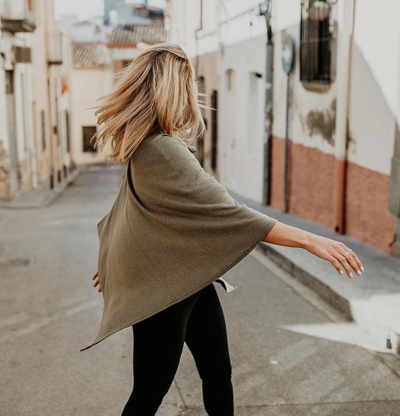 Peut inclure: Une femme portant un poncho vert et un legging noir marche dans une rue.