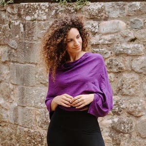 Peut inclure: Une femme portant un haut violet &agrave; col roul&eacute; avec des manches longues et un legging noir. Elle se tient devant un mur en pierre.